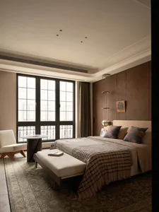Modern luxury bedroom featuring walnut wood paneling, a large bed with patterned pillows and striped throw, a white upholstered bench, and large grid windows with city view.