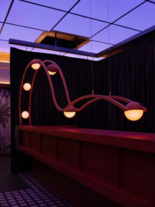 Modern reception desk made of walnut wood with a large, artistic, wavy pendant light fixture featuring multiple glowing spherical lamps against dark curtains and a purple ceiling.