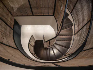 Looking down at a dramatic dark wood spiral staircase with intricate bamboo screen railings and walls, featuring a light-colored tiled floor visible at the bottom.