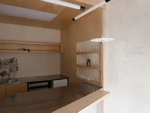 Modern minimalist kitchen with light oak cabinetry, dark reflective countertop, built-in appliances, open floating shelves, and contemporary pendant lighting.