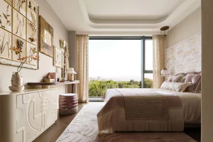 Modern serene bedroom interior with textured plaster wall, botanical framed art, large window overlooking green landscape, and upholstered bed with neutral linens.