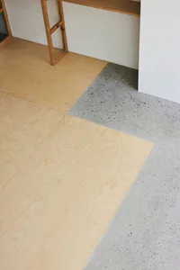 近拍淺色橡木地板與帶藍黑骨料的灰色水磨石之間無縫交接的細節。