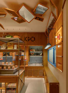 Lugo 麵包店內部空間，展示暖色木質櫃體、玻璃甜點展示櫃、色彩豐富的商品包裝，以及天花板上獨特的斜角木框鏡面裝置。
