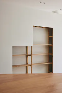 Modern minimalist living room featuring custom light oak built-in shelving units recessed into a white wall, with a solid oak table in the foreground.