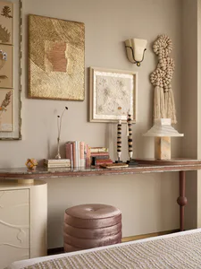 Elegant console table styled with textured gold and white wall art, marble lamp, velvet stool, and curated books against a neutral wall.