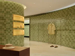 Modern dressing room featuring a curved wall covered in sage green ceramic tiles, built-in illuminated floating shelves, a clothing rack with a yellow shirt, and a wooden console with a straw hat in the foreground.